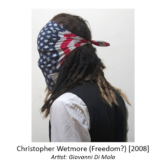 Person with dreadlocks, collared shirt, and vest with American flag cloth tied over face